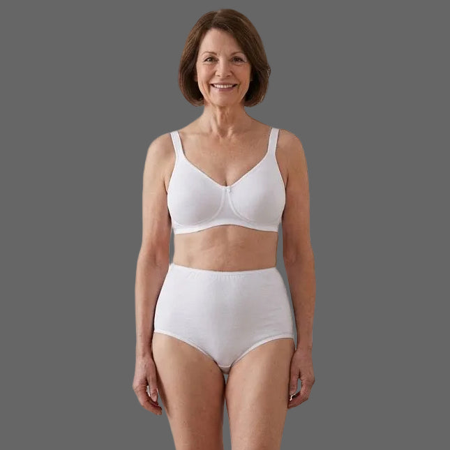 A smiling woman with short brown hair stands against a gray background, modeling the Teri Lingerie Full Coverage, Elastic Leg, Cotton Brief in white (Style 122), available in a convenient 4 pack.